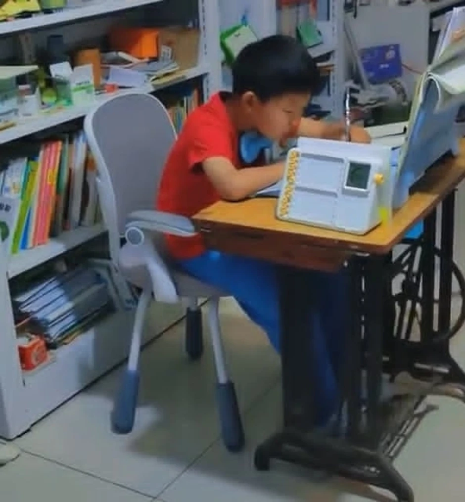 Cậu bé vừa đạp máy khâu vừa làm bài tập